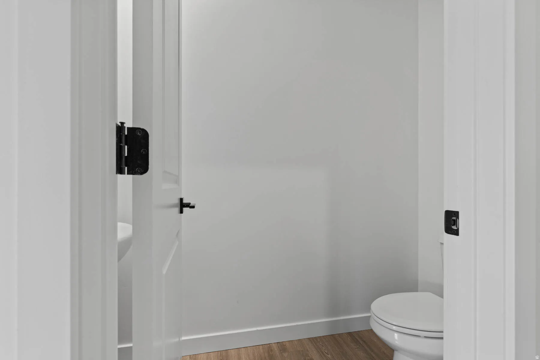 Powder room with wood-finish flooring, white walls, and a white toilet