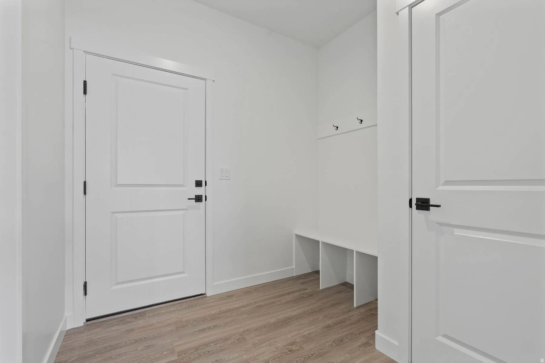 Entryway featuring light wood-finish flooring, white walls, and a built-in bench with storage cubbies and coat hooks