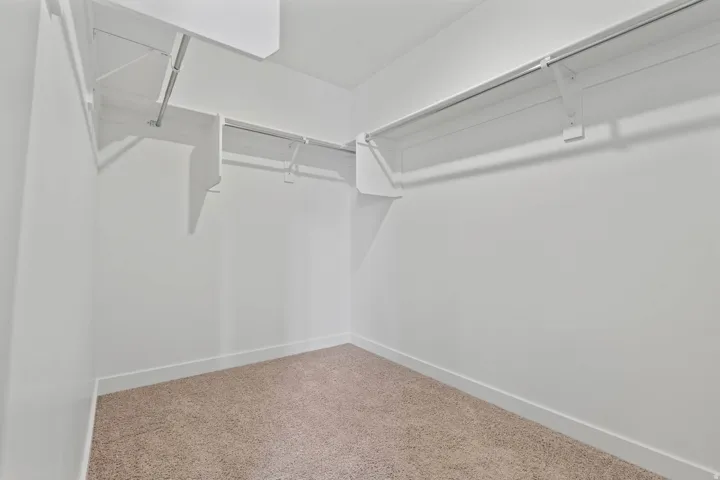 Walk-in closet featuring white wire shelving, metal hanging rods, light-colored carpet, white walls, and white baseboards