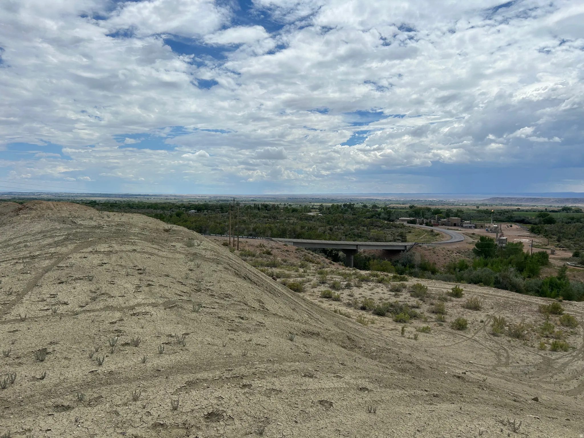 Elevated desert landscape featuring expansive terrain, distant green vegetation, and a bridge structure spanning a lower area
