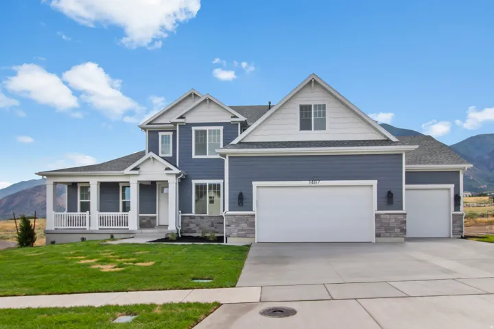 Contemporary residence featuring a blue siding exterior with white trim, a covered front porch, an attached multi-car garage, and a concrete driveway