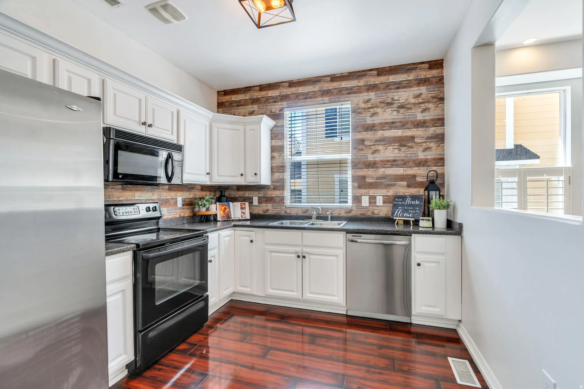 Kitchen featuring black appliances, white cabinetry, dark wood-type flooring, wooden walls, and dark stone countertops