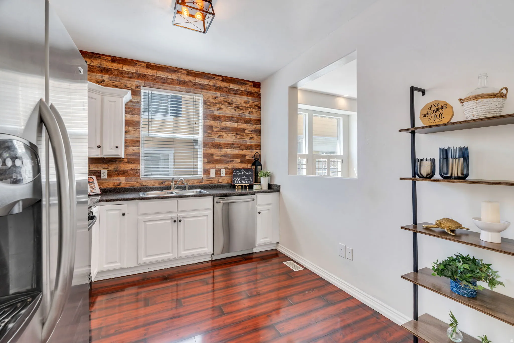 Kitchen with stainless steel appliances, white cabinets, wooden walls, and dark wood-style floors
