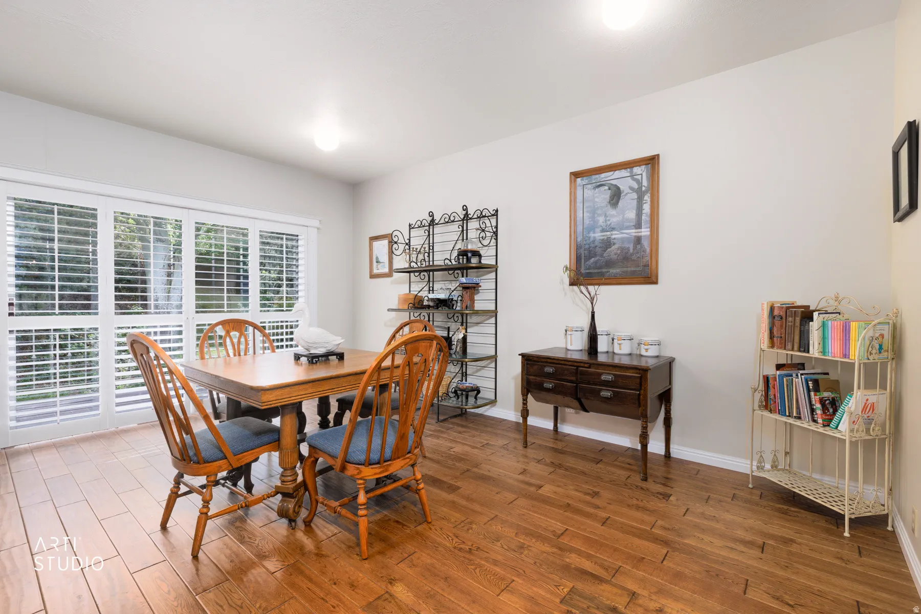 Interior space featuring rich wood-finish flooring, white walls, and a large multi-pane window with white plantation shutters
