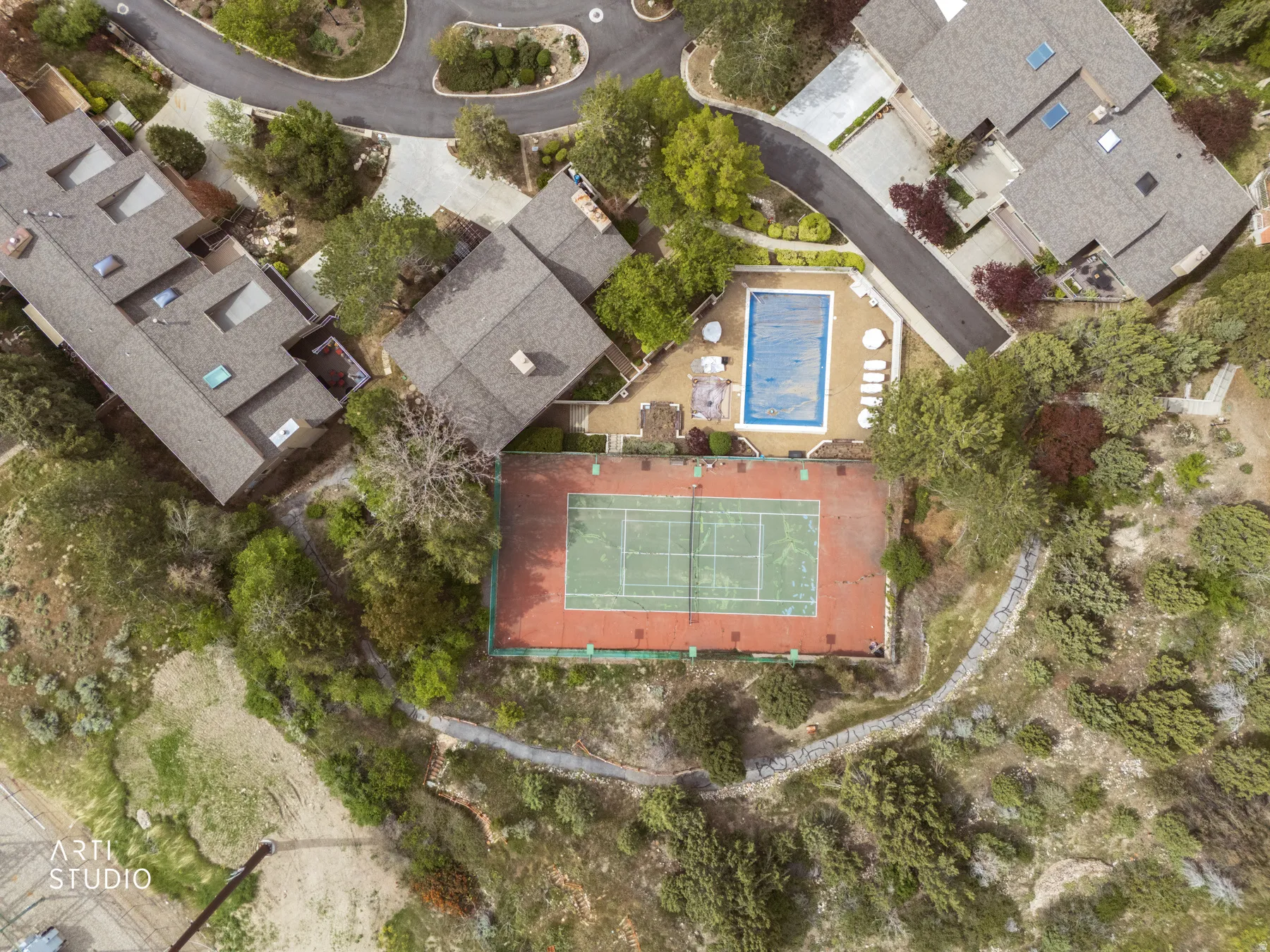 Aerial view of HOA club and pool area featuring a private tennis court with a red and green surface, a rectangular swimming pool