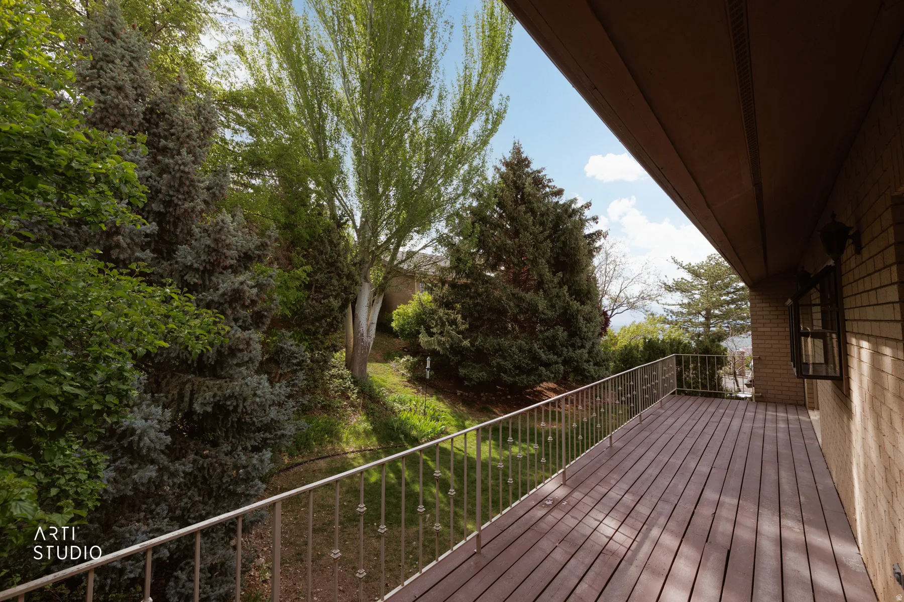 Spacious outdoor deck featuring wood-finish flooring, metal railing, and brick exterior wall