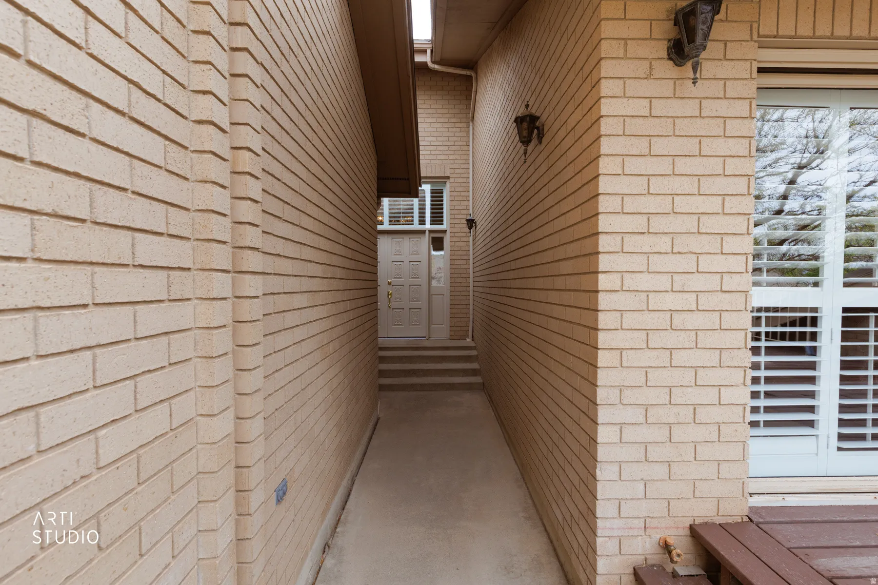 Entry walk-up featuring brick exterior, front door and plantation shutters visible in window.