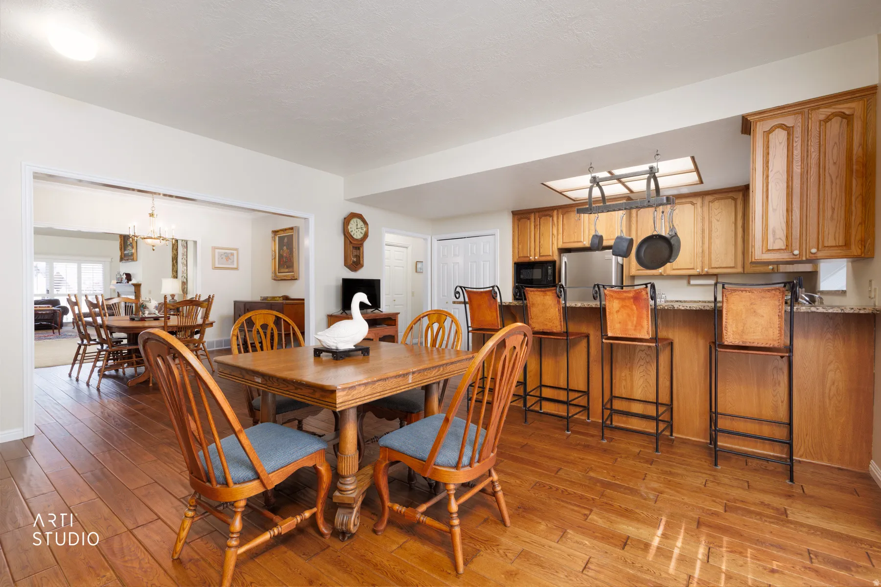 Open-concept living area featuring wood-finish flooring, a kitchen with light wood cabinetry, stainless steel appliances, a breakfast bar, and a skylight