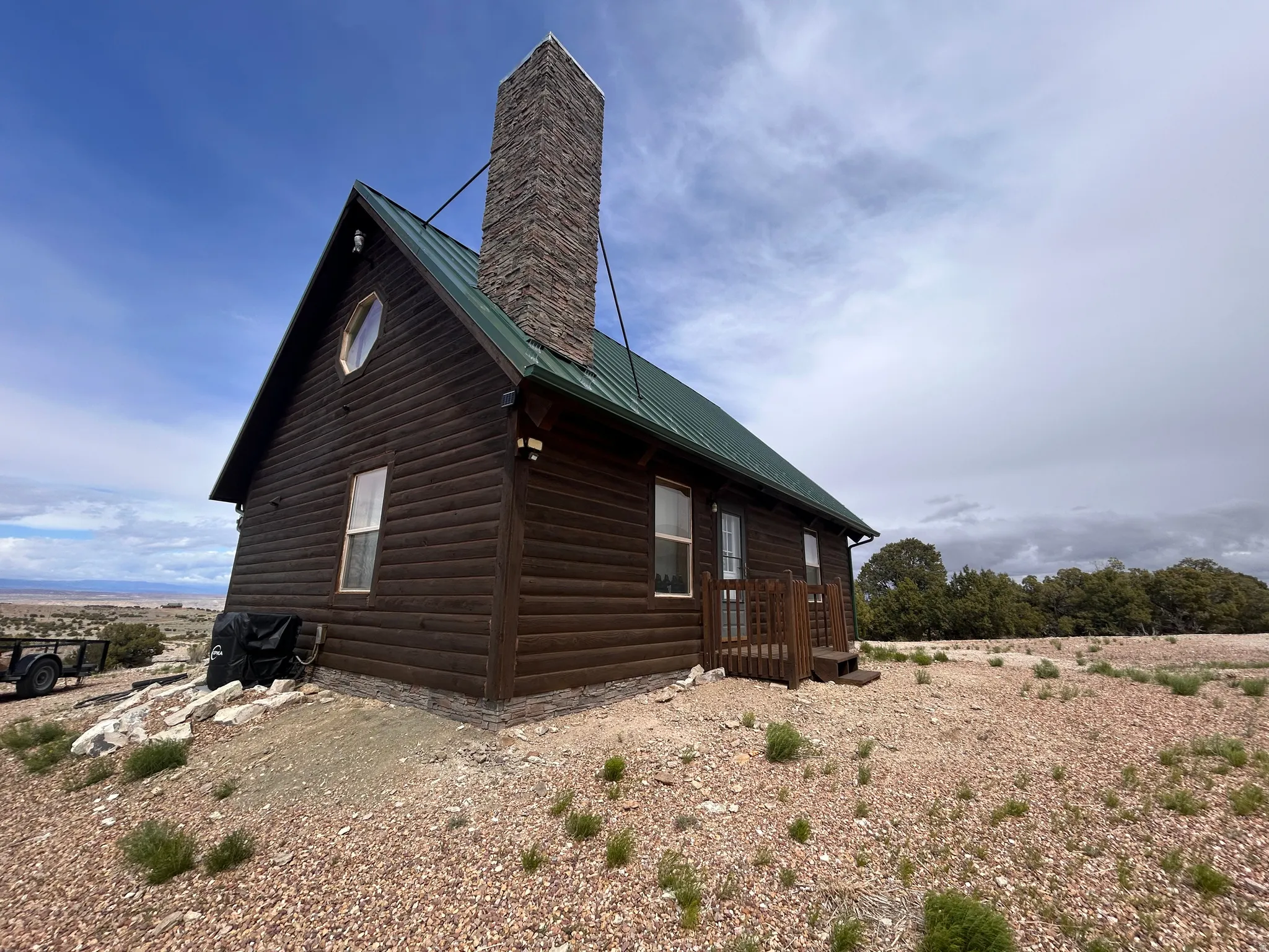 Log cabin exterior featuring a green metal roof, stone chimney, and wood siding