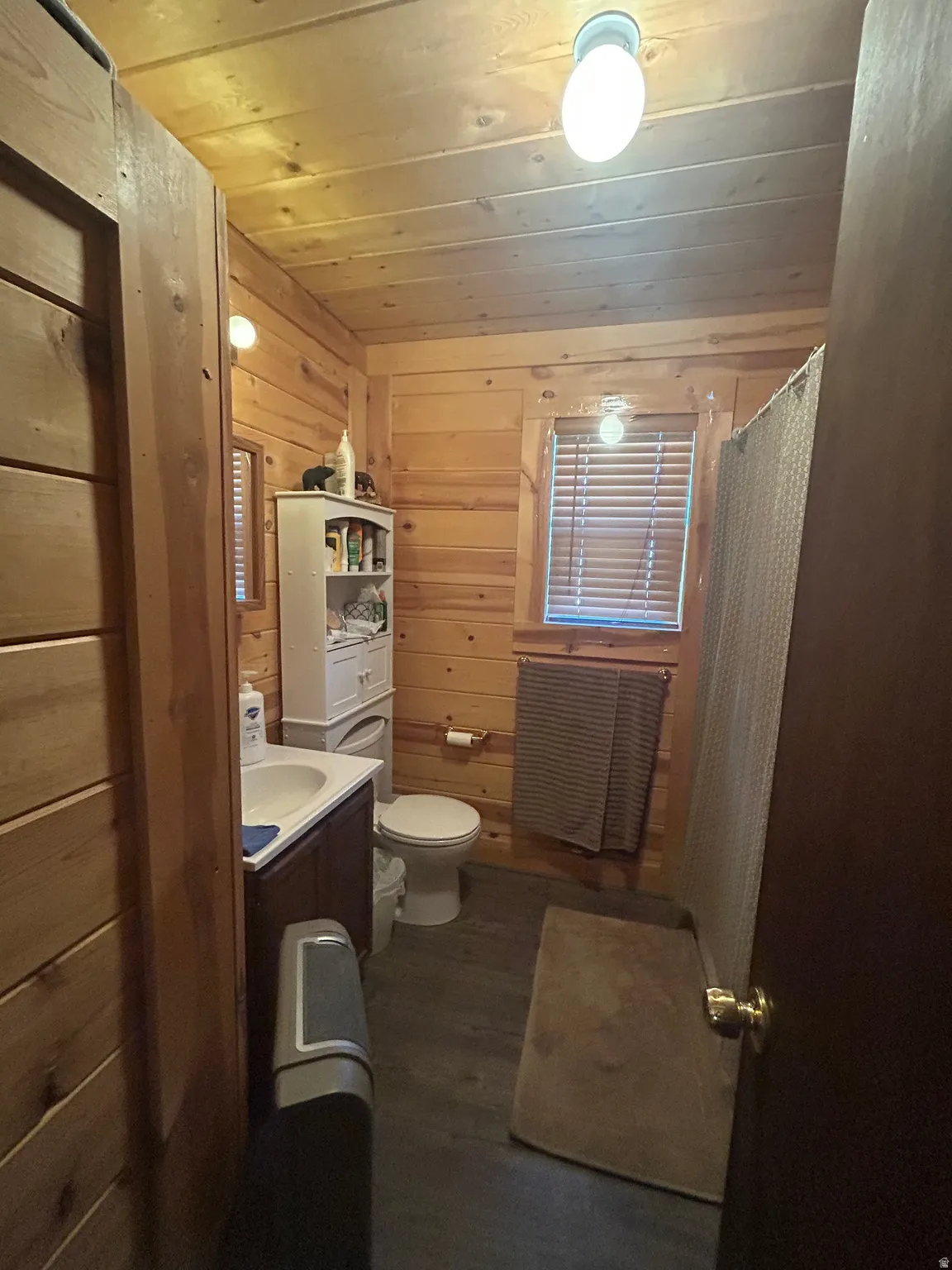 Wood-paneled bathroom featuring a dark wood vanity with an integrated sink, a toilet, a window with blinds, and wood-finish flooring