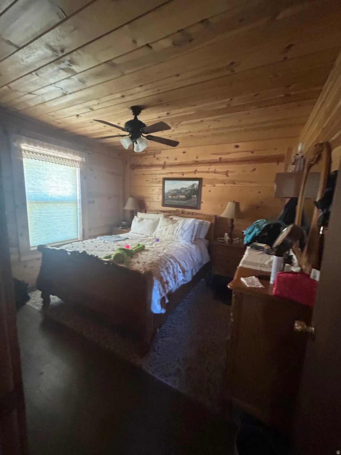 Bedroom featuring natural wood-paneled walls and ceiling, dark wood-finish flooring, and a ceiling fan with integrated lighting