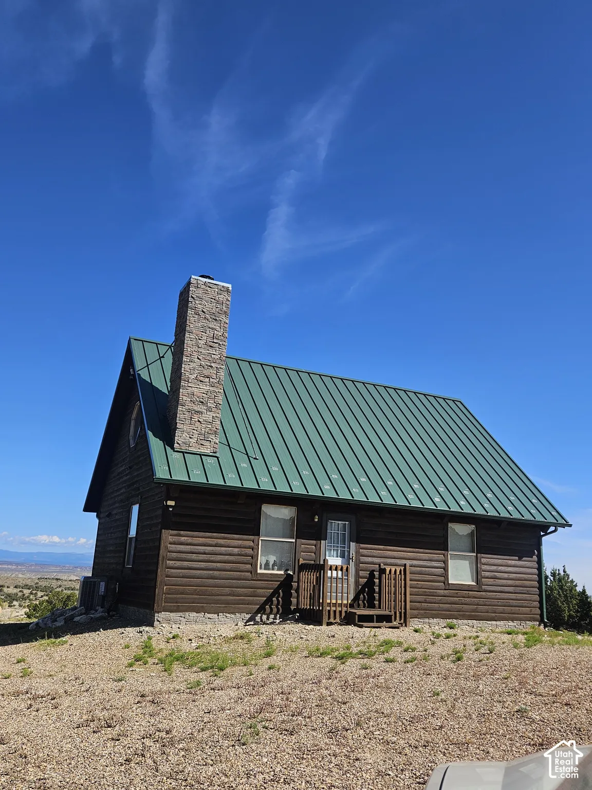 Log-sided exterior with a green metal roof, stone chimney, and an elevated porch
