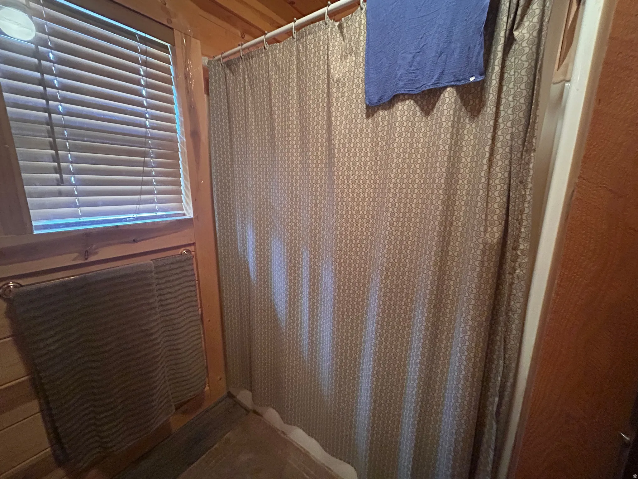 Shower enclosure with a patterned curtain, set against wood-finish wall paneling