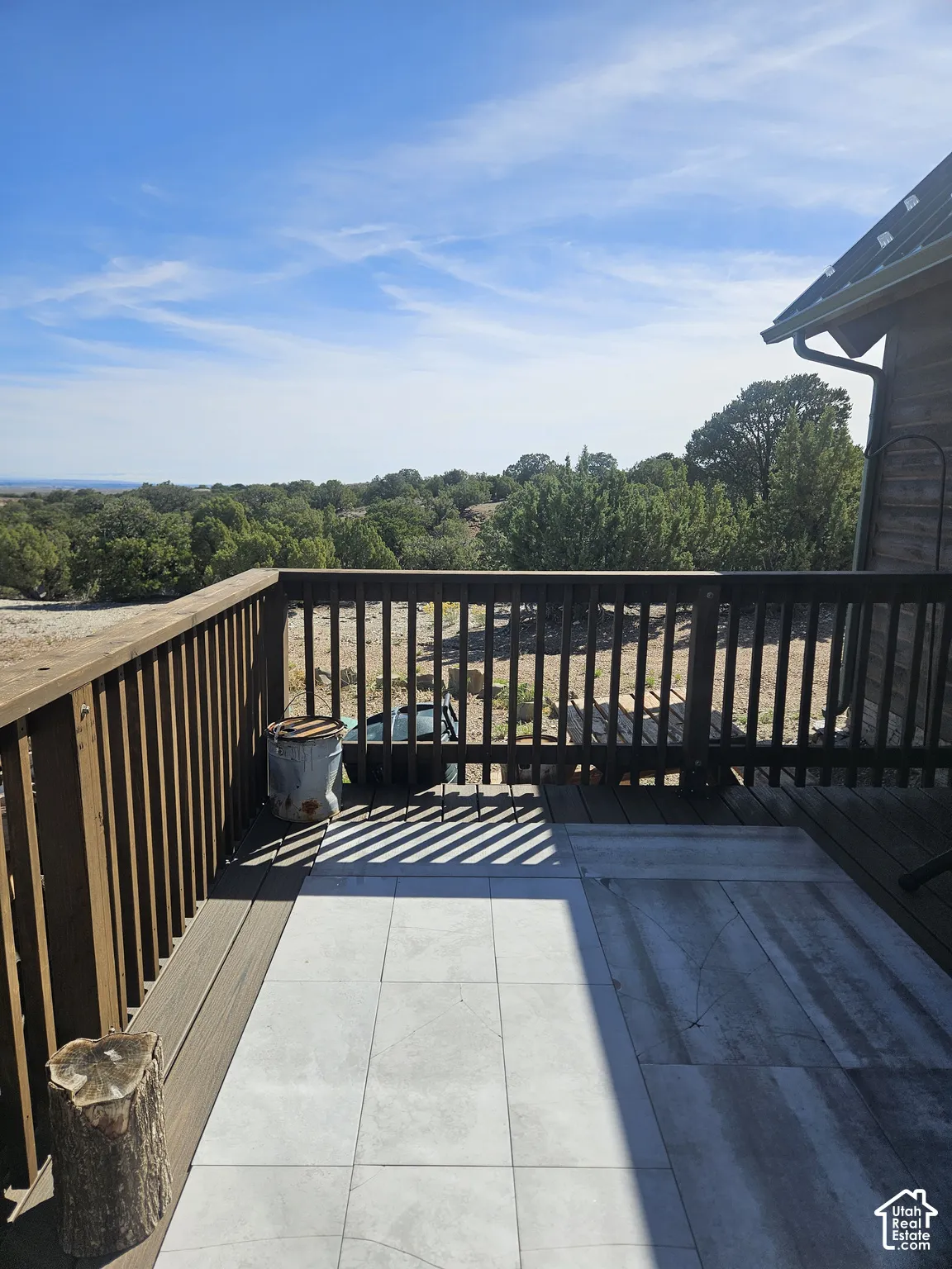 Deck with wood-finish railing and tile flooring, offering expansive tree-lined scenery