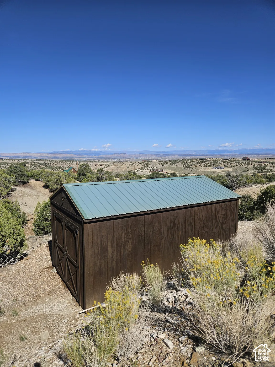 Storage shed with a green metal roof and wood-finish siding, positioned on a sloped terrain