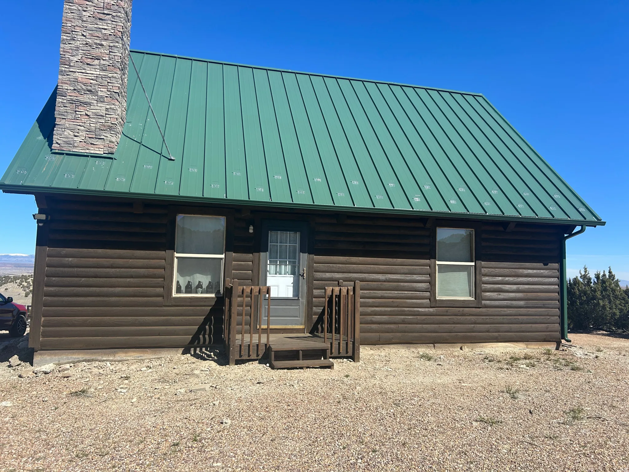 Log cabin exterior featuring a green metal roof, stone chimney, and wood siding