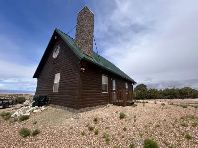 Log cabin exterior featuring a green metal roof, stone chimney, and wood siding