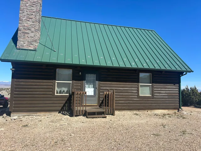 Log cabin exterior featuring a green metal roof, stone chimney, and wood siding
