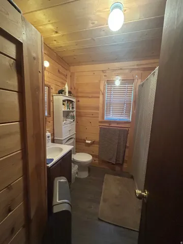 Wood-paneled bathroom featuring a dark wood vanity with an integrated sink, a toilet, a window with blinds, and wood-finish flooring