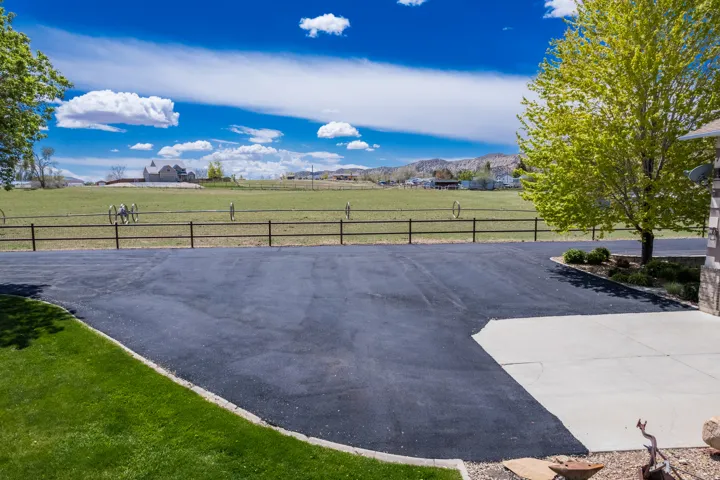 Expansive asphalt driveway with a concrete pad and surrounding green lawn