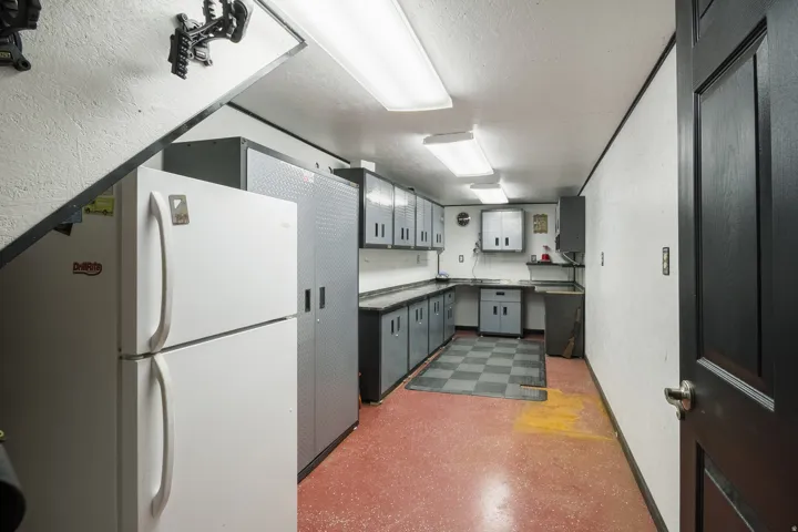 Utility room featuring extensive cabinetry, fluorescent overhead lighting, a built-in sink, and a durable red flooring finish