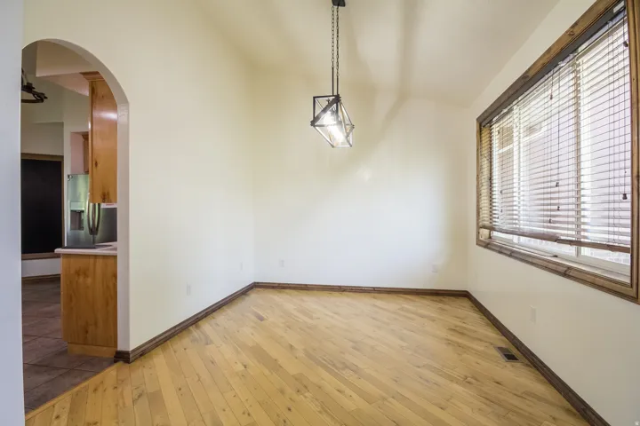 Bright room featuring wood-finish flooring, a large window with wood-finish blinds, a modern geometric pendant light fixture, and an arched doorway