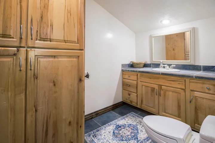 Bathroom featuring natural wood cabinetry, a built-in vanity with an undermount sink, blue tile countertop with matching backsplash, and blue tile flooring