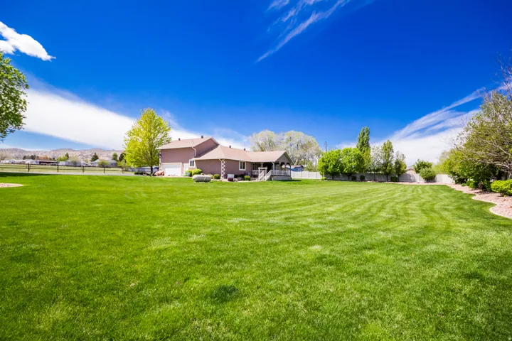 Expansive green lawn with a residential structure featuring a gable roof, an attached garage, and a rear deck