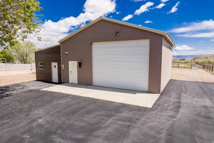 Detached auxiliary building featuring a large white roll-up door, two entry doors, and a separate side structure with horizontal wood-finish siding