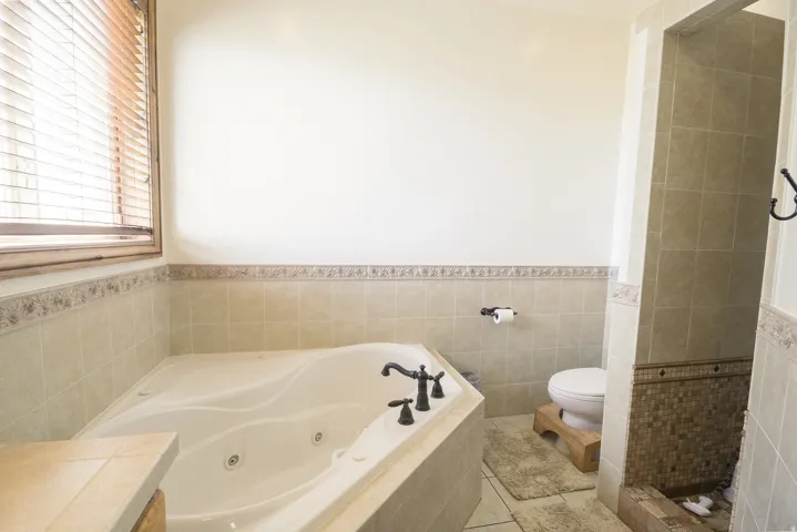 Soaking tub with bronze-finish fixtures, surrounded by light-toned tilework and a decorative border