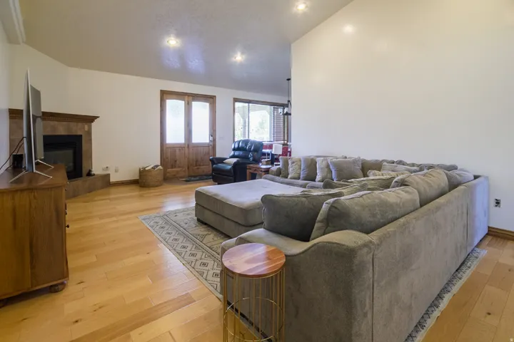Spacious living area featuring wood-finish flooring, a corner fireplace with a tiled surround, recessed lighting, and double wood doors with frosted glass panels