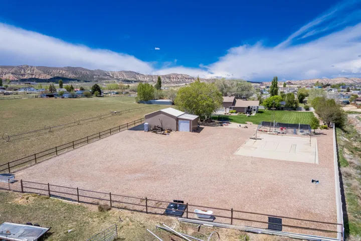 Expansive property featuring a large gravel-surfaced area, a dedicated sand court, and a detached outbuilding