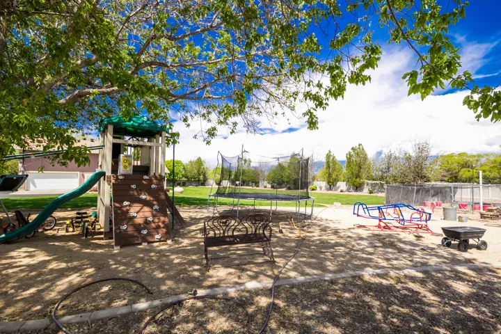 Spacious outdoor area featuring a play structure with slide and climbing wall, a trampoline, and a wide grassy expanse