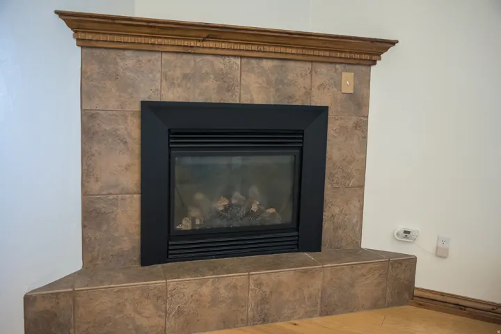 Gas fireplace with a black metal frame, surrounded by large format ceramic tiles and topped with a decorative wood mantel