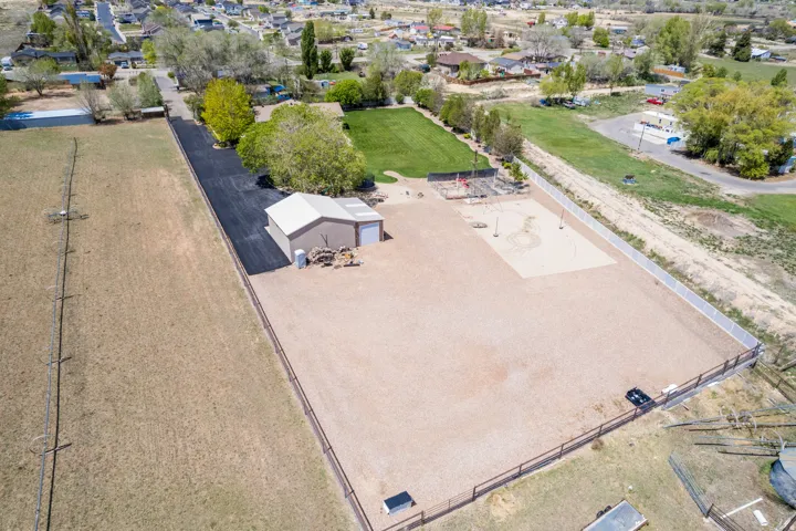 Expansive property featuring a large gravel area, a detached outbuilding with a roll-up door, a section of manicured lawn, and a sand court