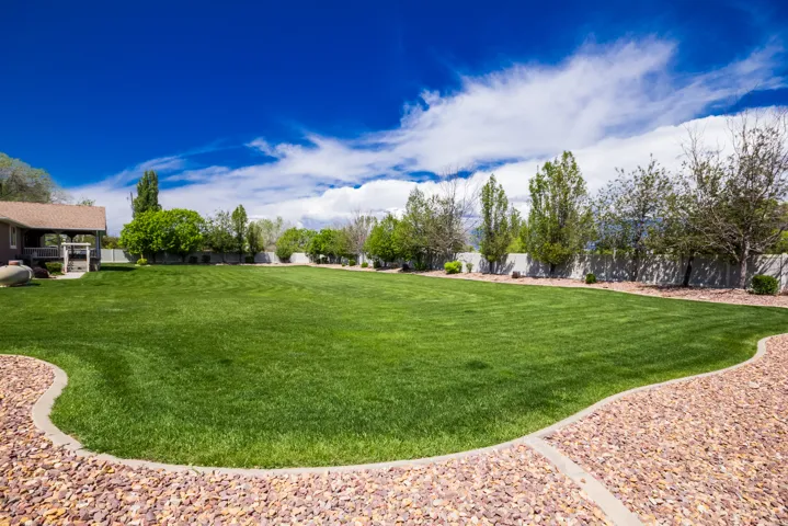 Expansive green lawn with a defined gravel perimeter, mature trees, privacy fencing, and a multi-level deck structure visible in the background