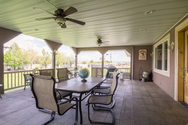 Spacious covered patio featuring a wood-finish stamped concrete floor, multiple ceiling fans, recessed lighting, and a white-framed window
