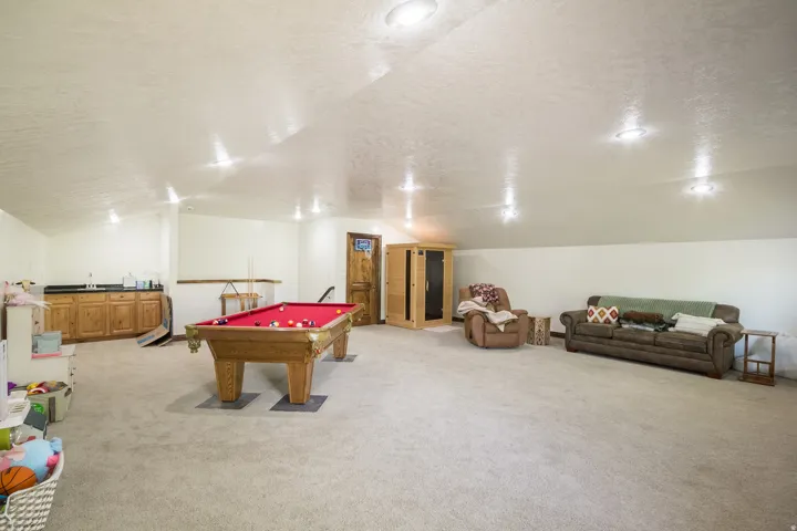 Spacious recreation room featuring recessed lighting, light-toned carpeting, a built-in wood-finish wet bar with upper countertop, and a wood-finish interior sauna