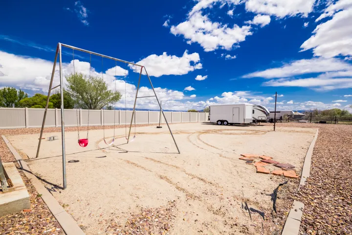 Expansive outdoor area featuring a swing set with two swings, a gravel border, and a sand-filled play space