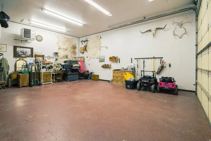 Spacious garage with a durable concrete floor, overhead fluorescent lighting, and a wall-mounted heater