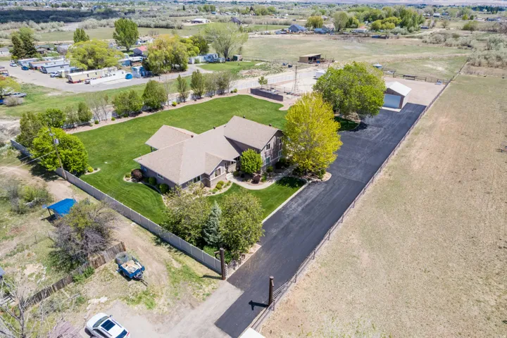 Spacious property featuring a large residence with a brown shingled roof, extensive manicured lawn, paved driveway, mature trees, and a detached outbuilding