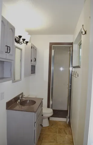 Bathroom featuring a glass-enclosed shower, light-toned vanity with an integrated sink, wall-mounted lighting fixture, and tiled flooring