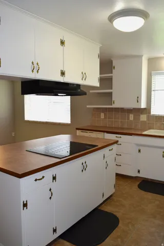 Kitchen featuring an island with a built-in cooktop, white cabinetry with decorative brass hardware, brown countertops, and coordinating tile flooring