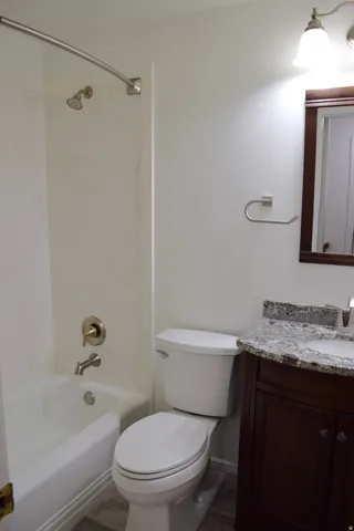 Bathroom featuring a white tub with brushed nickel fixtures, a white toilet, and wood-finish flooring