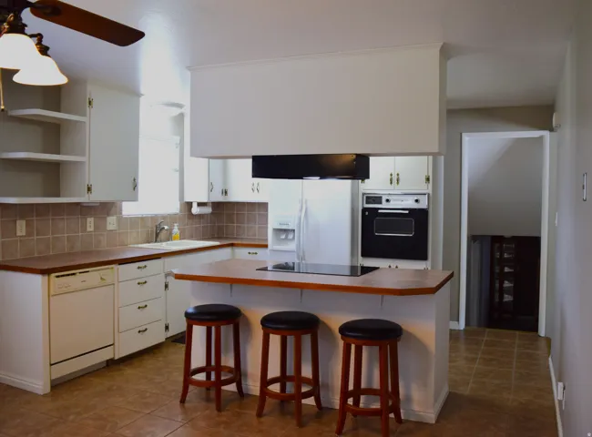 Kitchen featuring an island with a built-in cooktop, white cabinetry, a built-in oven, tile flooring, and a ceiling fan