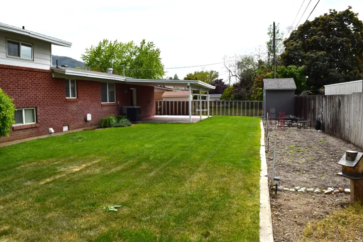 Expansive backyard featuring a manicured lawn, a covered patio, and a storage shed