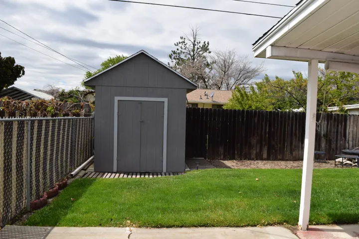 Backyard featuring a gray utility shed on a wood slat base, a chain-link fence, and a wooden privacy fence