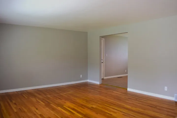 Spacious room with wood-finish flooring, white baseboards, and a wide cased opening to an interior room