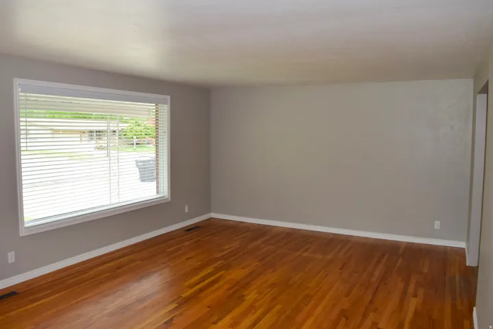 Expansive room featuring wood-finish flooring, white baseboards, and a large window with horizontal blinds