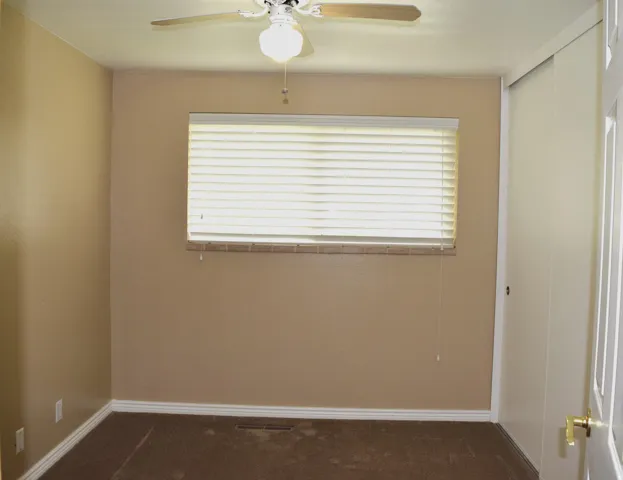 Bedroom featuring a ceiling fan with integrated lighting, a window with horizontal blinds, tan walls, and brown carpet flooring